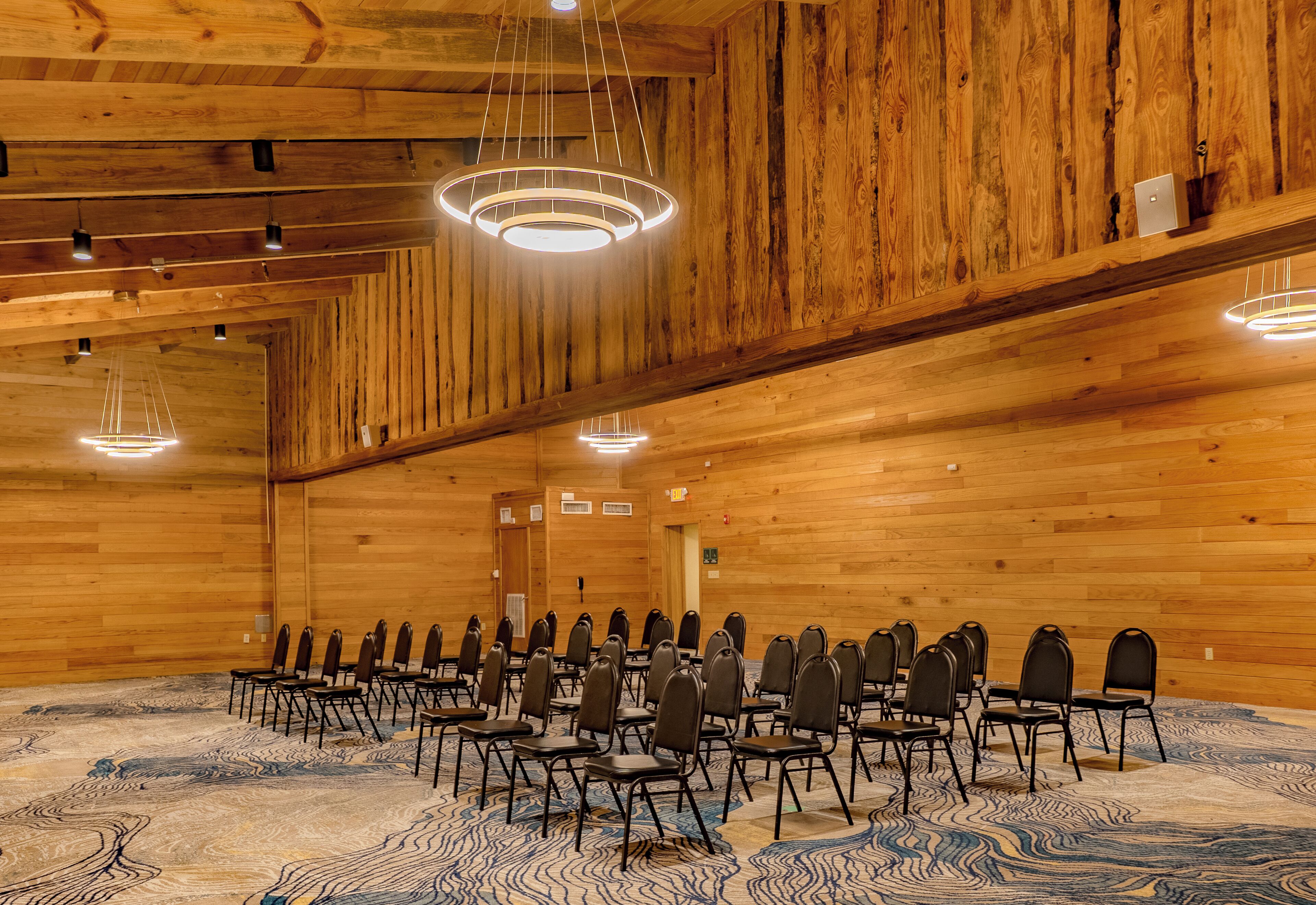 Ein Konferenzraum mit Holzwänden und -decke, Reihen von Stühlen und modernen Leuchten.