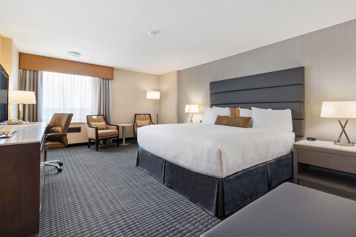 Une chambre d’hôtel avec un grand lit, un bureau, deux chaises et une table de chevet avec une lampe.