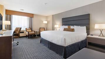Habitación de hotel con una cama grande, un escritorio, dos sillas y una mesita de noche con lámpara.