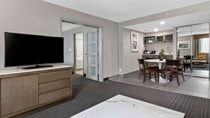 A modern hotel room with a flat-screen TV, a marble coffee table, a dining area with a round table and chairs, and a kitchen area with a microwave and cabinets. - Best Western Premier Calgary Plaza Hotel & Conference Centre (Calgary)
