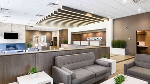 A modern reception area with a grey sofa, white tables, and a flat-screen TV. - Best Western Premier Calgary Plaza Hotel & Conference Centre (Calgary)