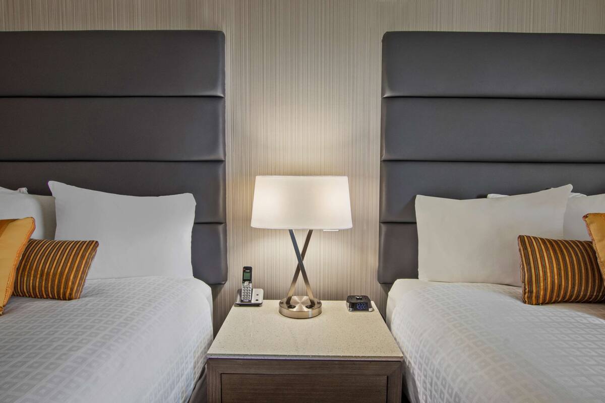 Une chambre d’hôtel avec deux lits, une table de chevet avec une lampe, un téléphone et une horloge numérique.