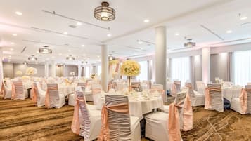 A spacious banquet hall with round tables, white chairs, and floral centerpieces.