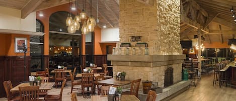 A restaurant with wooden tables and chairs, stone walls, and hanging light fixtures.