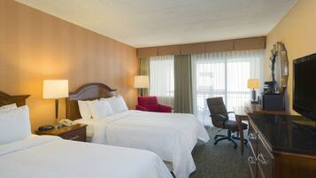 A hotel room with two beds, a desk with a television, a chair, and a desk lamp.