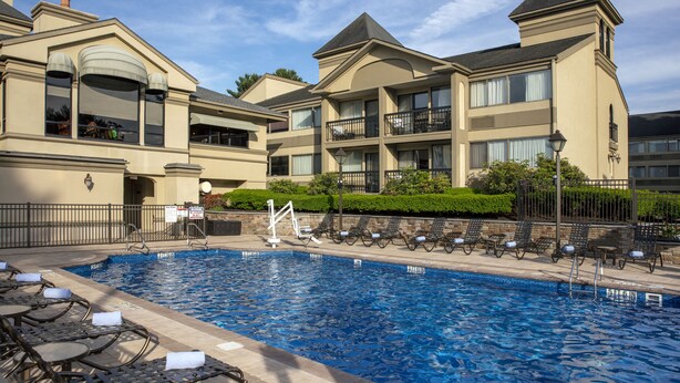 A hotel with a swimming pool, lounge chairs, and a well-maintained garden area.