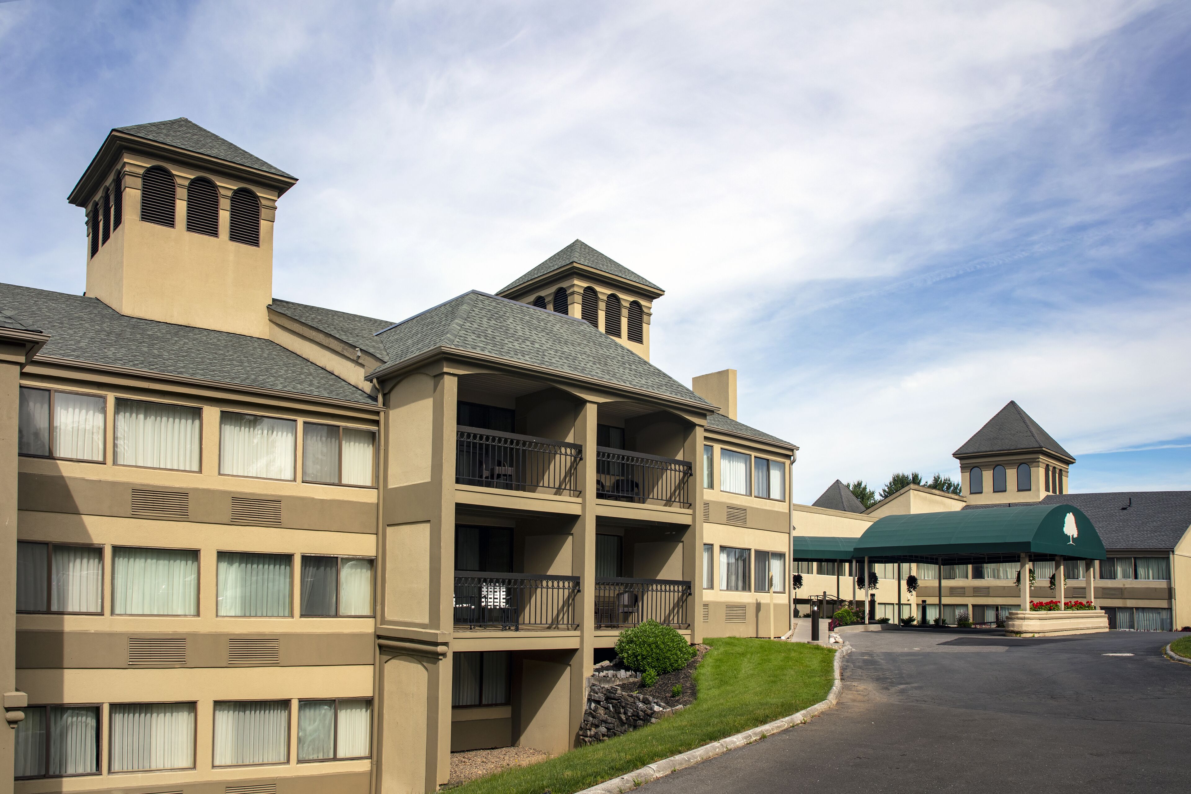 A multi-story hotel with balconies, a covered entrance, and a landscaped driveway.