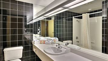 Une salle de bain moderne avec un lavabo blanc, un grand miroir et des murs recouverts de carreaux noirs.