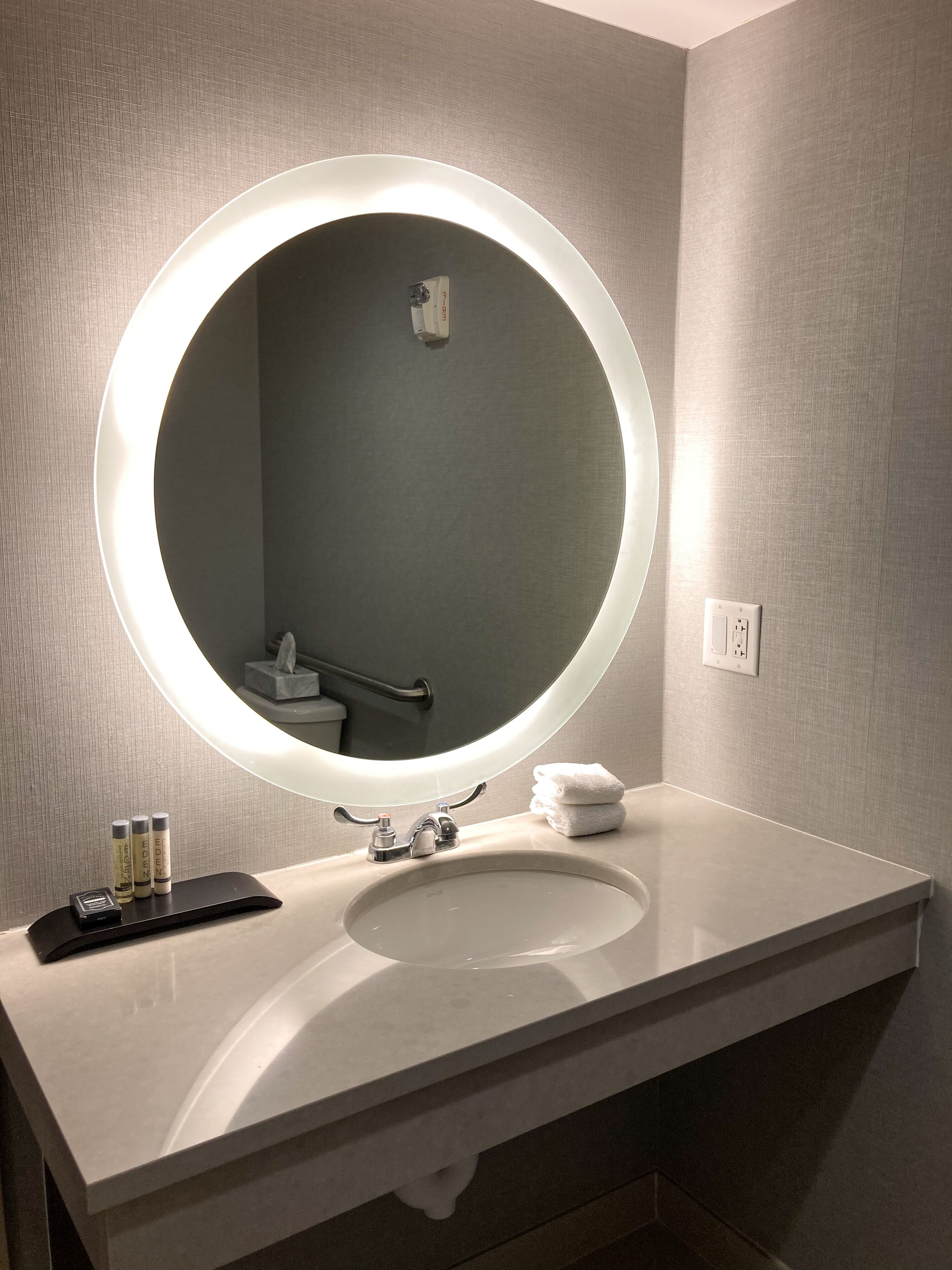 A bathroom with a round mirror, a sink, and a towel stack.