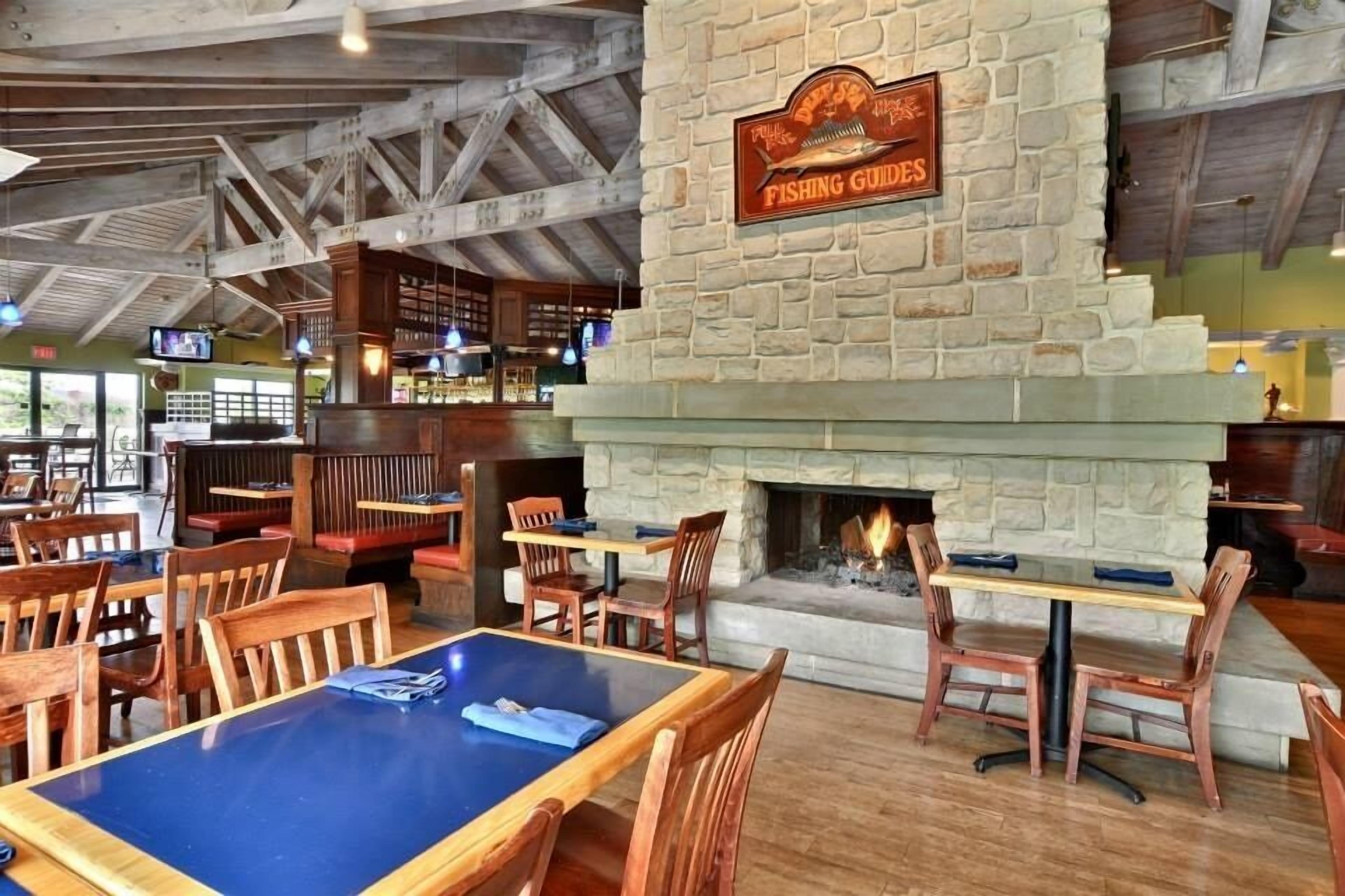 Interior de restaurante con chimenea de piedra, mesas y sillas de madera, y un cartel que dice 'FISHING GUIDES'.