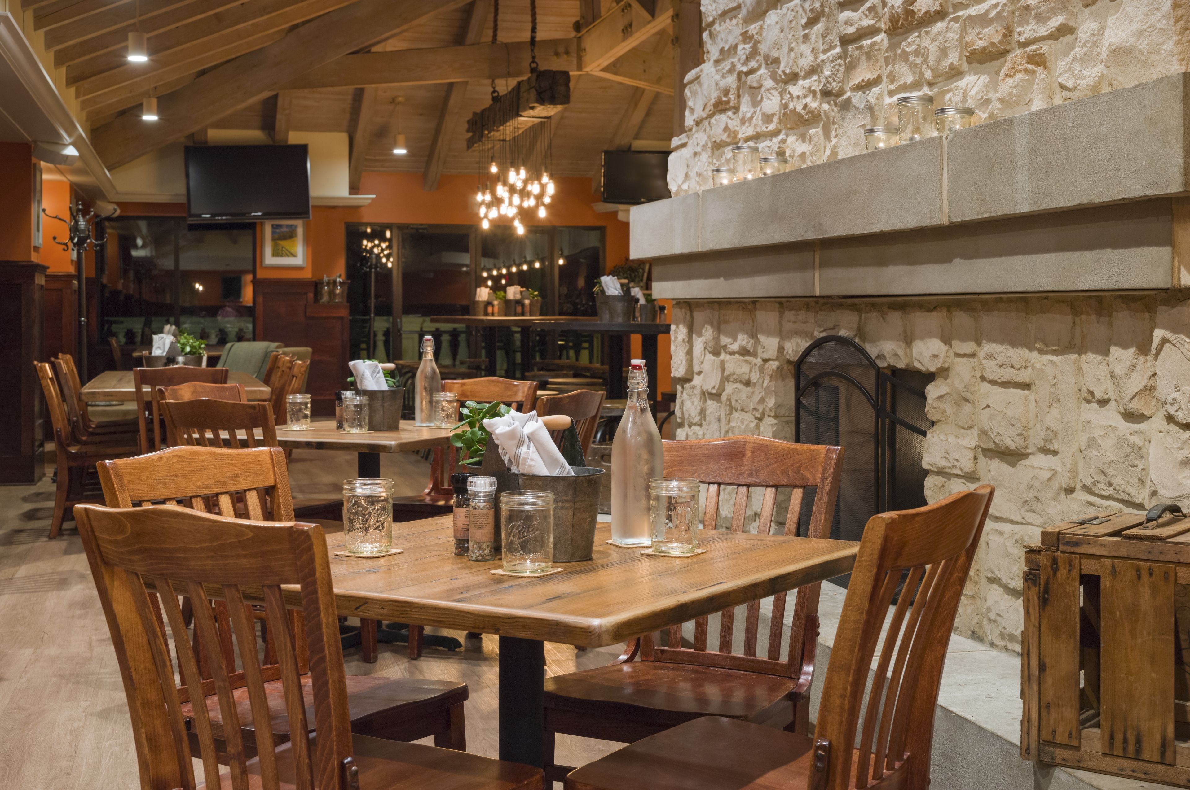 A restaurant with wooden tables and chairs, stone walls, and a fireplace.