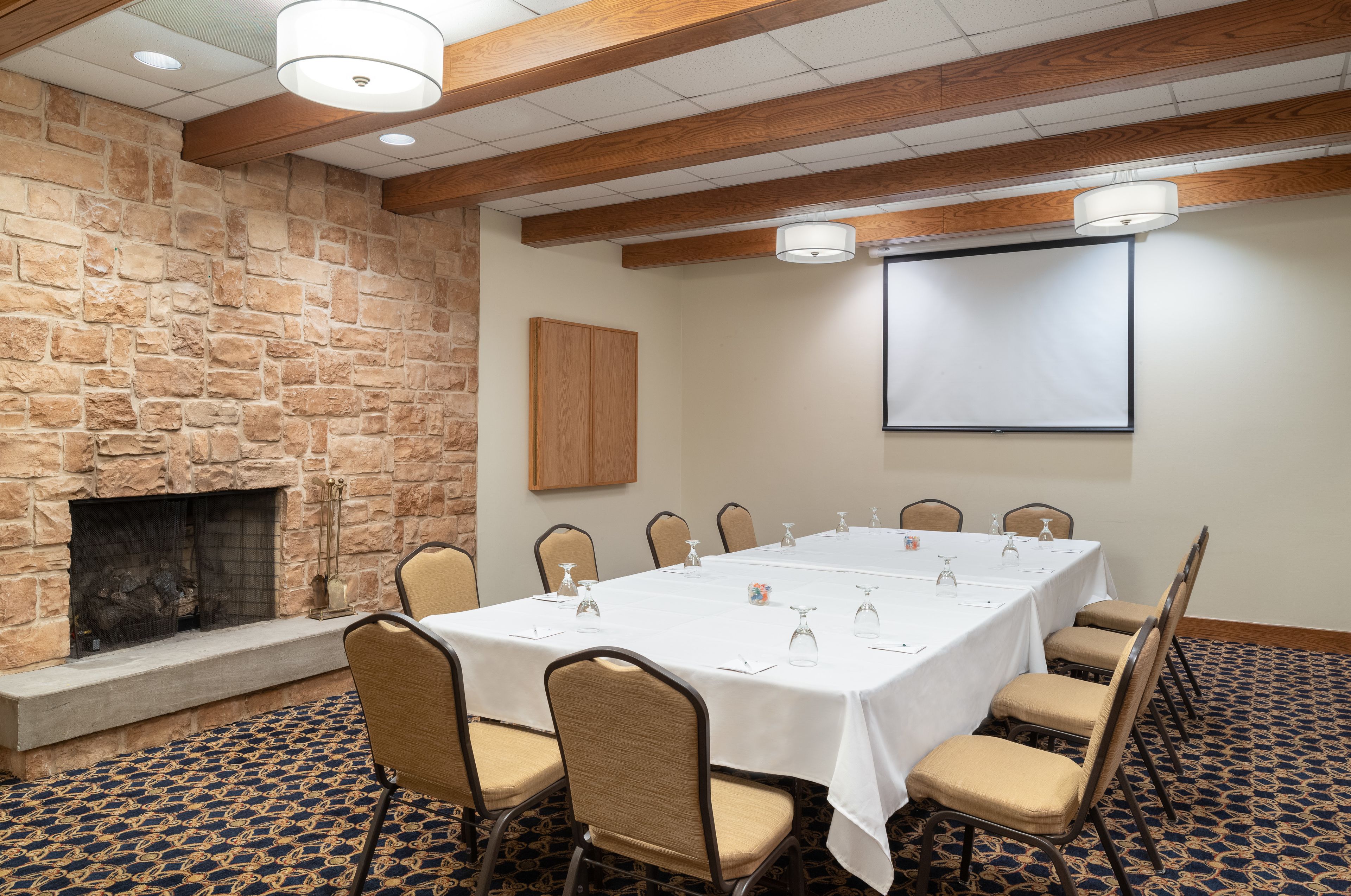 A conference room with a stone wall, fireplace, and a projector screen.