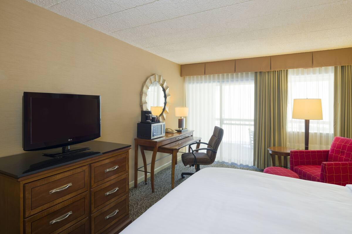 A hotel room with a bed, a desk with a computer, a television, a chair, and a lamp.