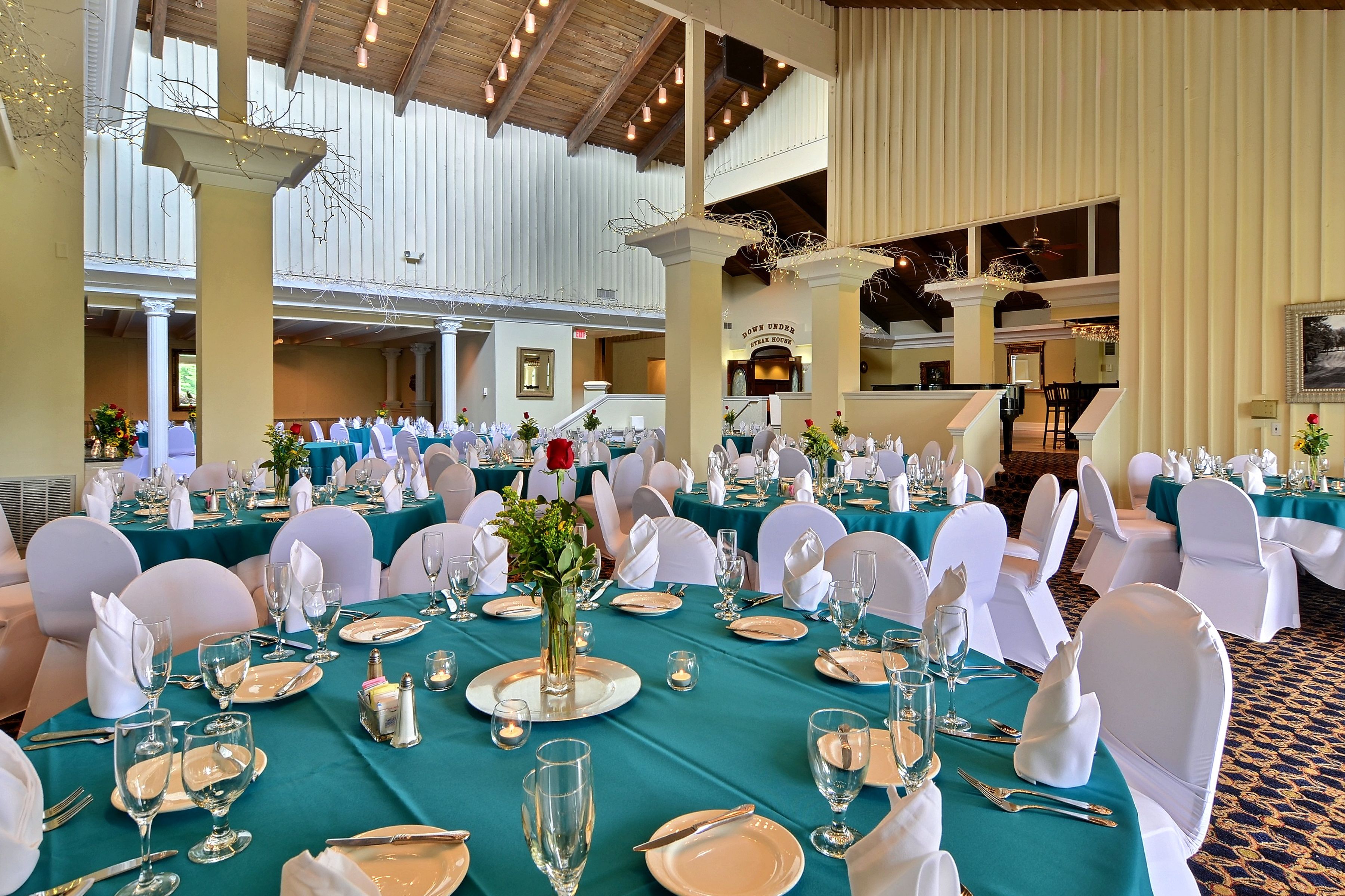 A banquet hall with teal tablecloths, white chairs, and a high ceiling with exposed beams.