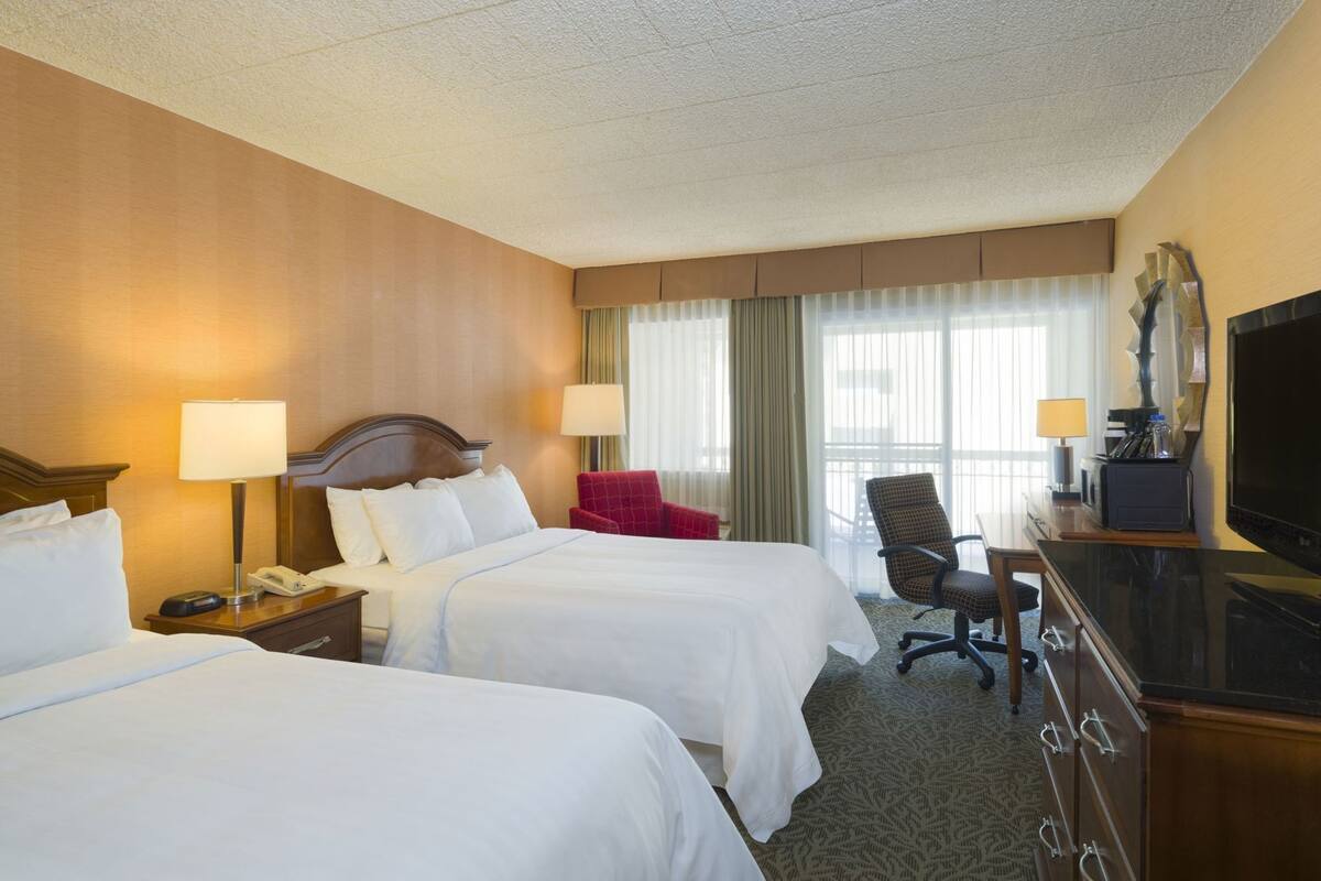 A hotel room with two beds, a desk with a TV, a chair, and a lamp.