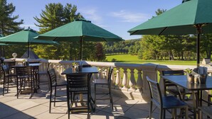 Un patio al aire libre con mesas y sillas, sombrillas verdes y vistas a un campo de golf.