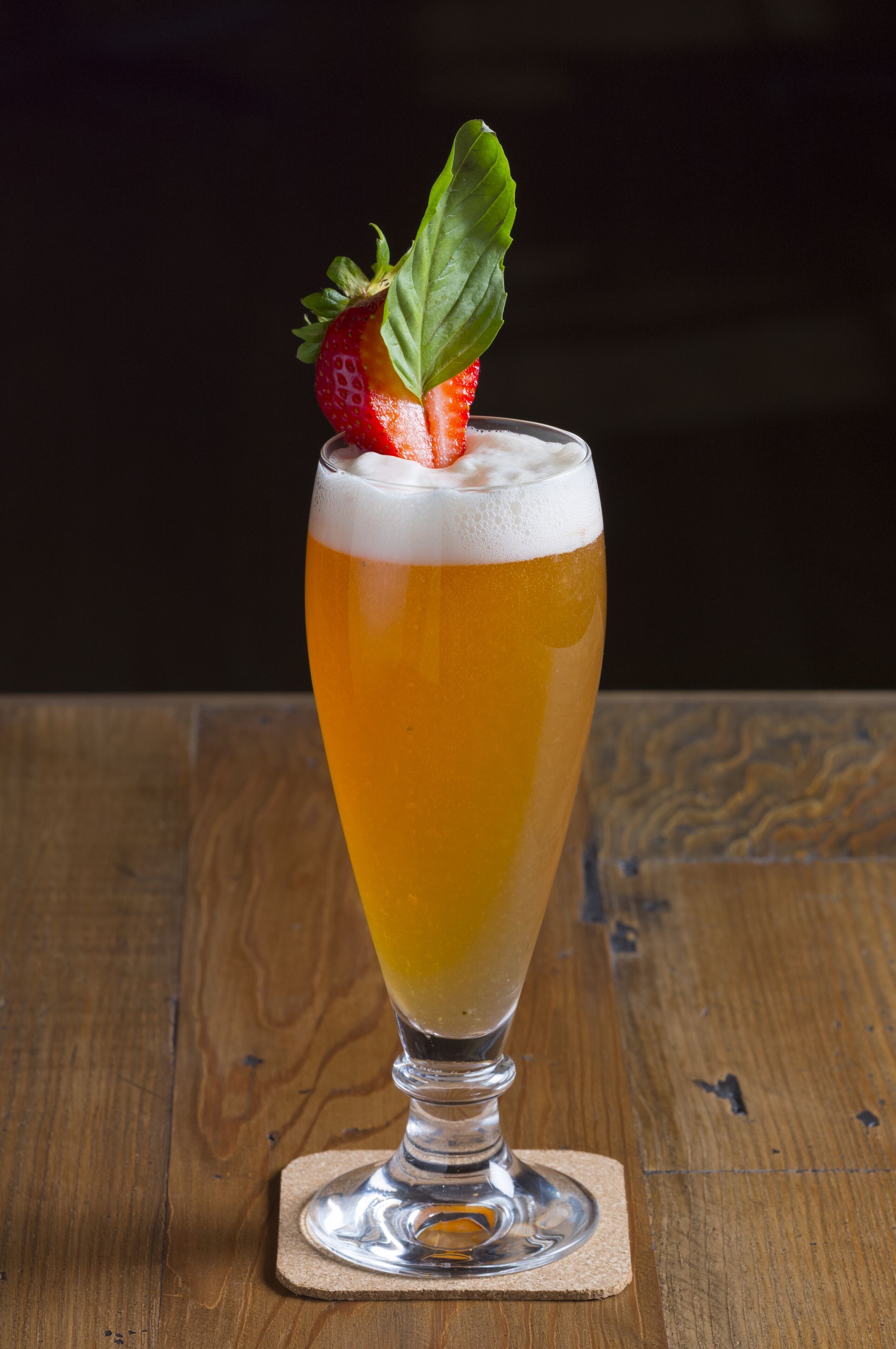 Un grand verre de bière, garni d’une fraise, posé sur un dessous de verre.