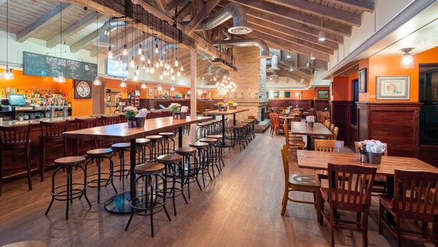 Un restaurante espacioso con techos altos, vigas a la vista y diversas opciones de asientos, como taburetes de bar y mesas.