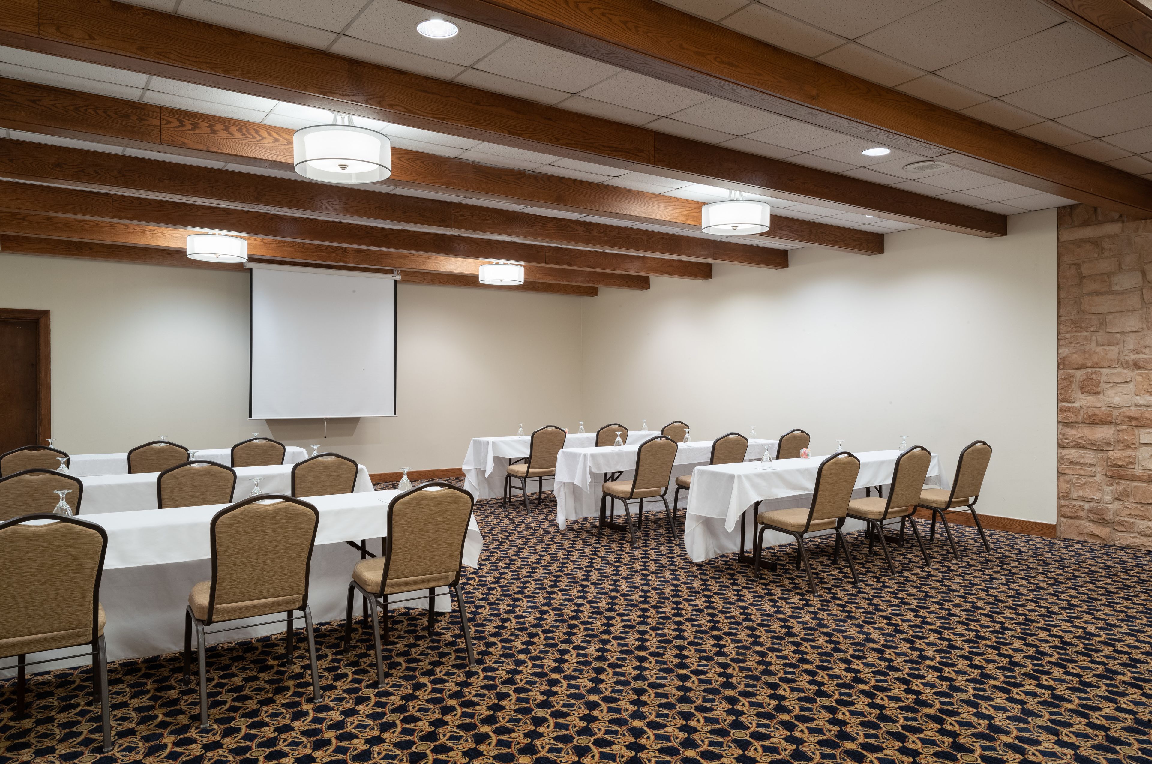 A conference room with tables and chairs, a projector screen, and a patterned carpet.