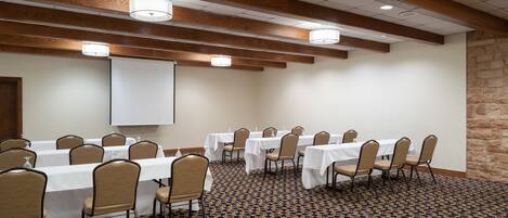 A conference room with tables and chairs, a projector screen, and a patterned carpet.