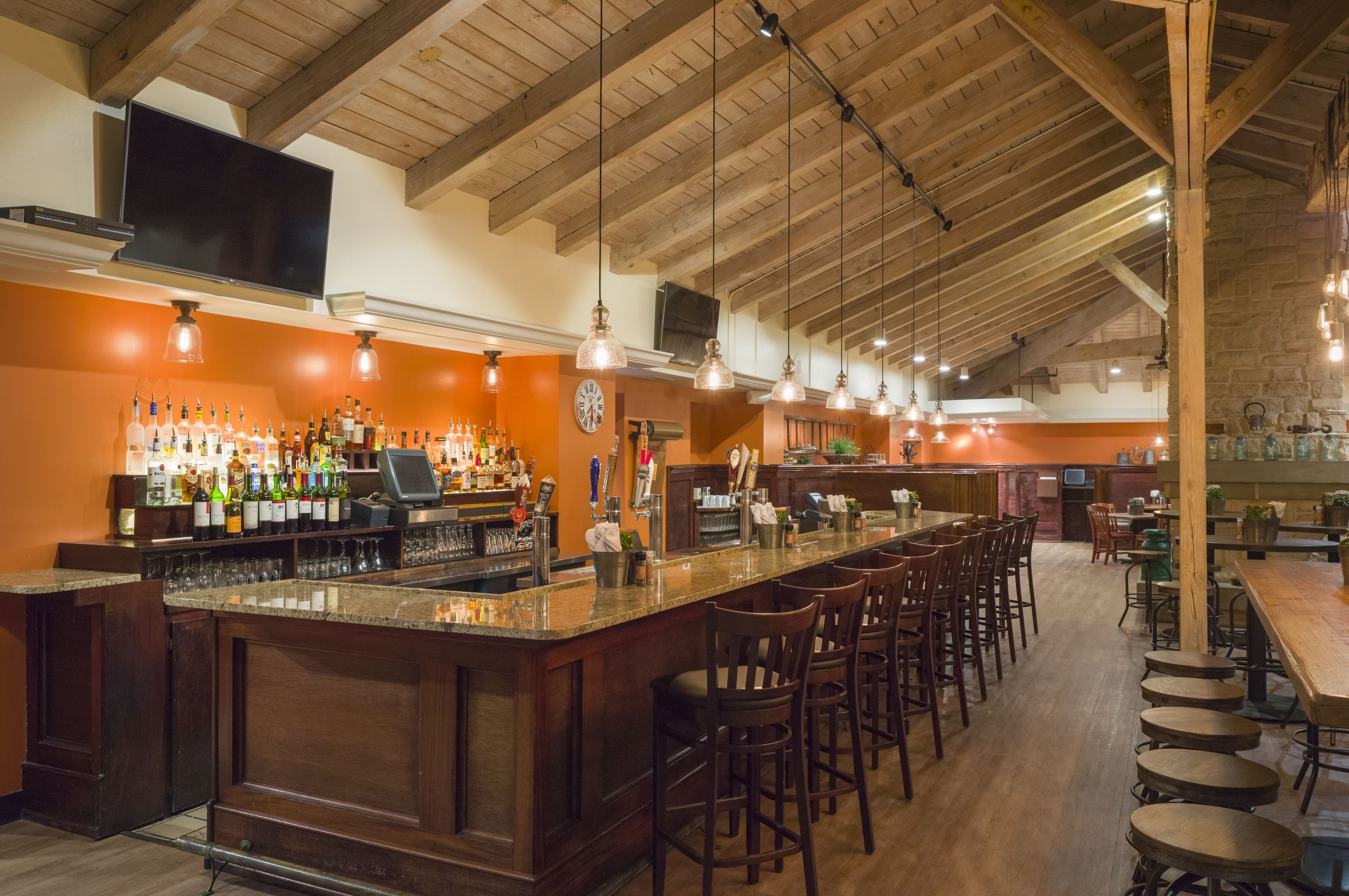 Uma área de bar com um balcão comprido, vários bancos e uma variedade de garrafas e copos.