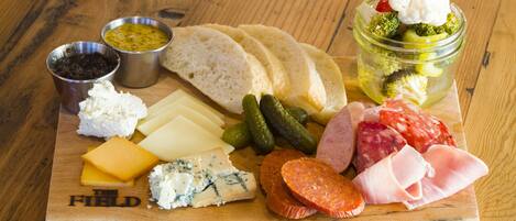 Une planche en bois garnie de différents fromages, de charcuteries et de cornichons.