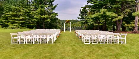 A grassy outdoor area with rows of white chairs arranged for an event.