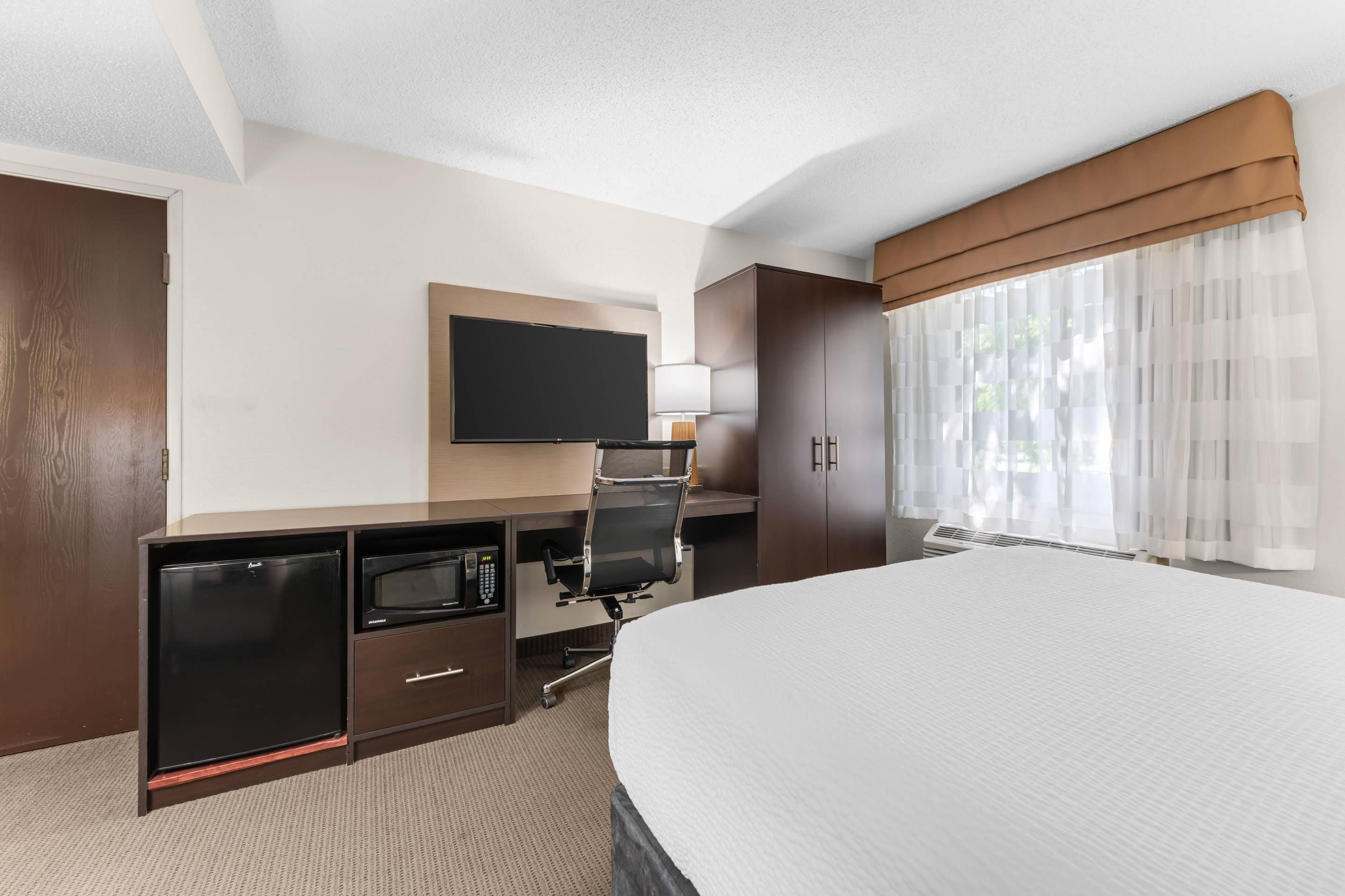 Ein Hotelzimmer mit einem Bett, einem Flachbildfernseher, einem Schreibtisch mit Mikrowelle und einem Fenster mit transparenten Vorhängen.