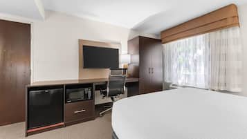 Quarto de hotel com cama, televisão de tela plana, escrivaninha com micro-ondas e janela com cortinas finas.