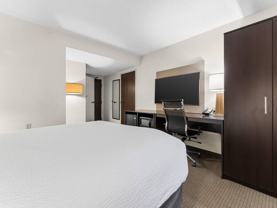 A hotel room with a large bed, a desk with a chair, a desk lamp, a flat-screen TV, and a wardrobe.