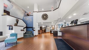 A hotel lobby with a staircase, a reception desk, and a large wall clock.