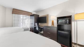 A hotel room with two beds, a desk, a chair, a television, a microwave, and a lamp.
