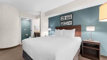 A hotel room with a bed, bedside tables, a nightstand, a wall-mounted lamp, and a door leading to a bathroom.