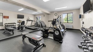 Une salle de sport équipée de divers appareils d’exercice, d’un miroir et d’un téléviseur.
