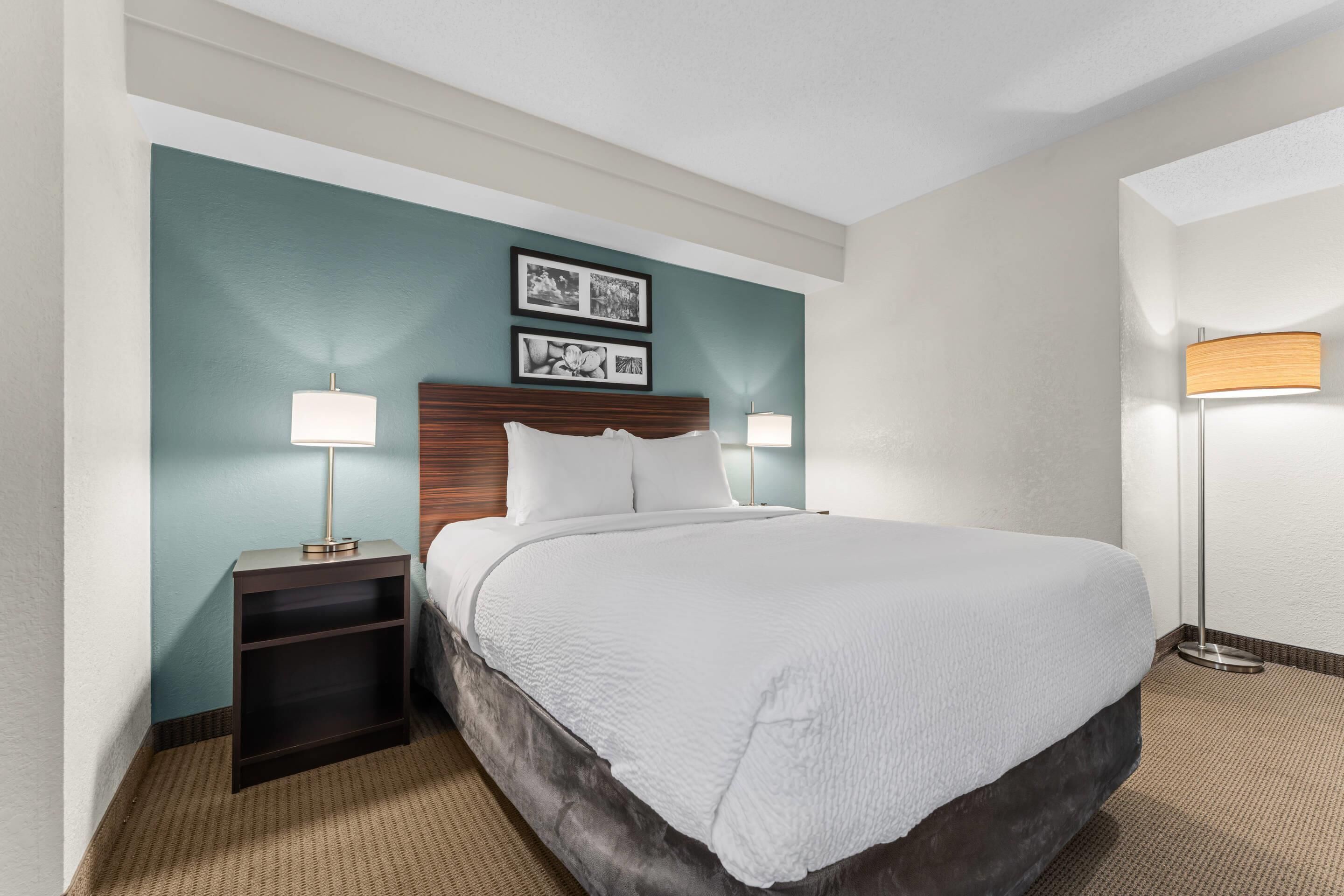A hotel room with a large bed, two bedside lamps, a nightstand, and two framed pictures on the wall.
