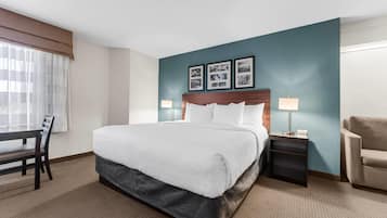 A hotel room with a bed, a desk, a chair, a nightstand, and a lamp.