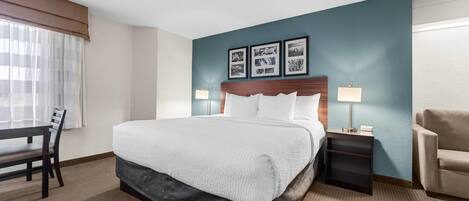 A hotel room with a bed, a desk, a chair, a nightstand, and a lamp.