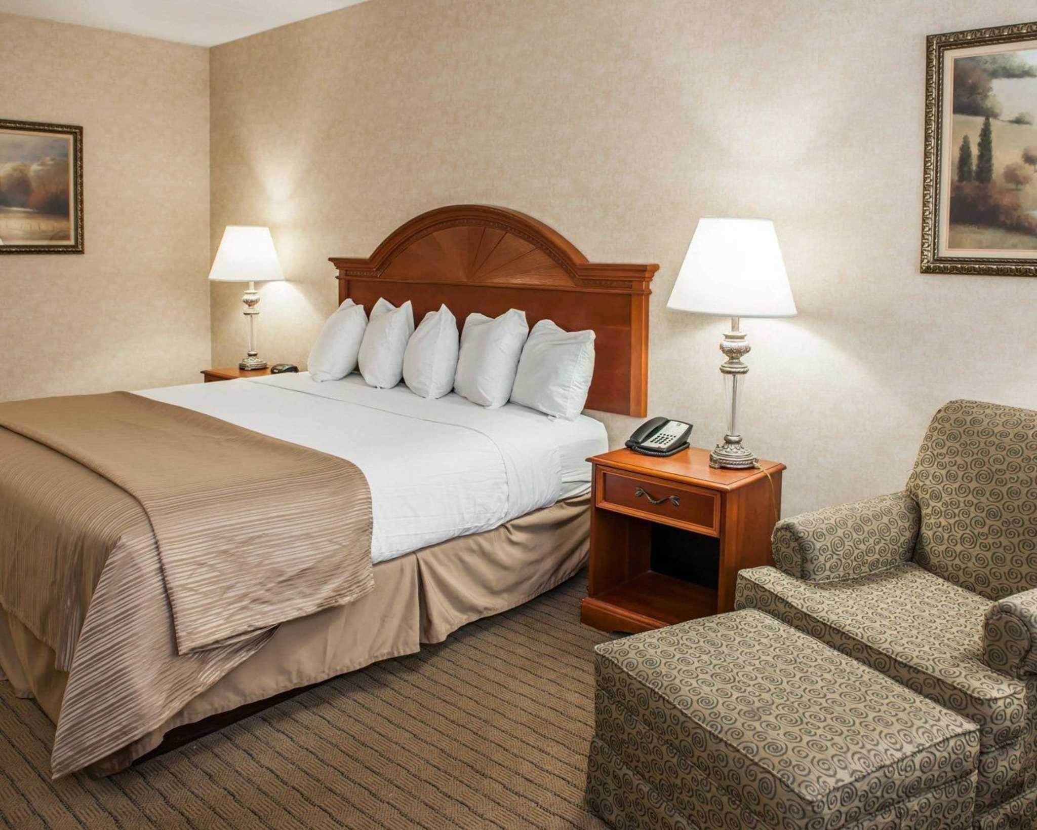 A hotel room with a bed, two bedside tables with lamps, a telephone, and a patterned armchair.