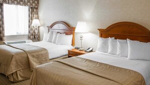Habitación de hotel con dos camas, cada una con cabecero de madera, ropa de cama blanca y mesita de noche con lámpara y teléfono.