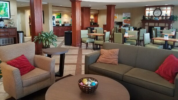 Un hall de hotel con una zona de estar central, una cocina al fondo y un reloj en la pared.