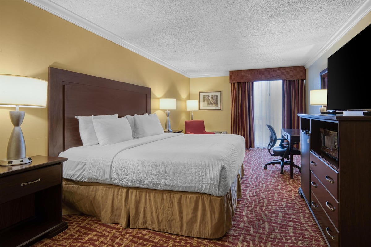 A hotel room with a large bed, a desk with a computer, a TV, and a minibar.