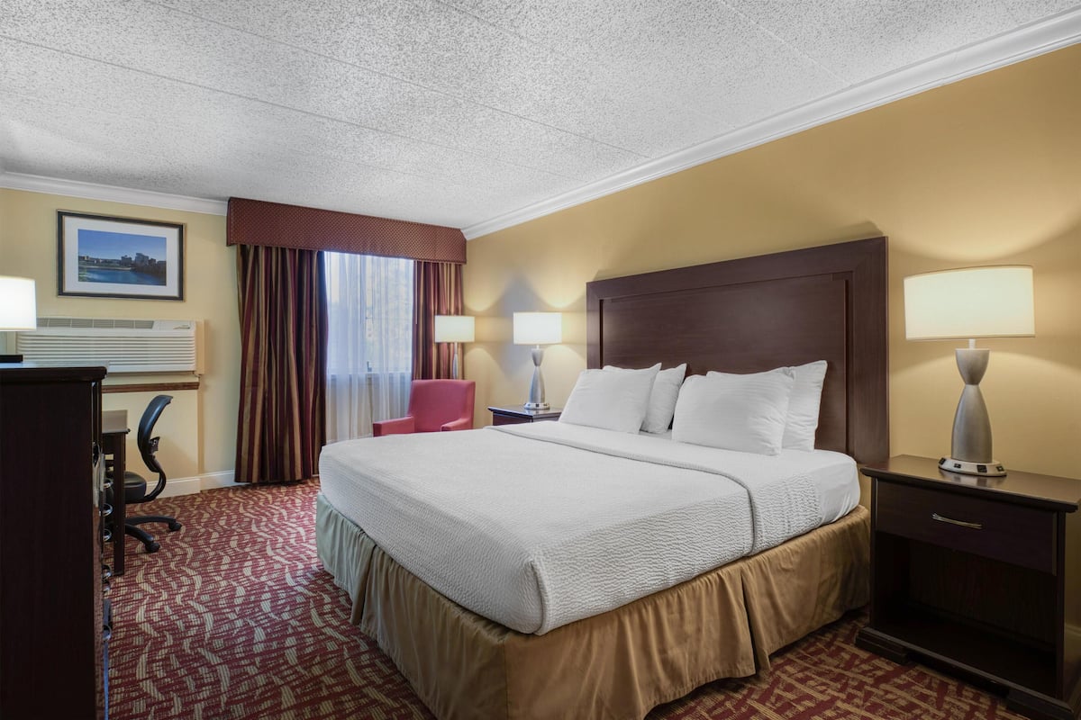 A hotel room with a large bed, two bedside lamps, a desk with a chair, and a framed picture on the wall.