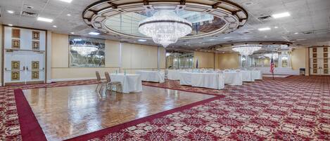 A spacious ballroom with a large chandelier, white tables, and a red carpet.