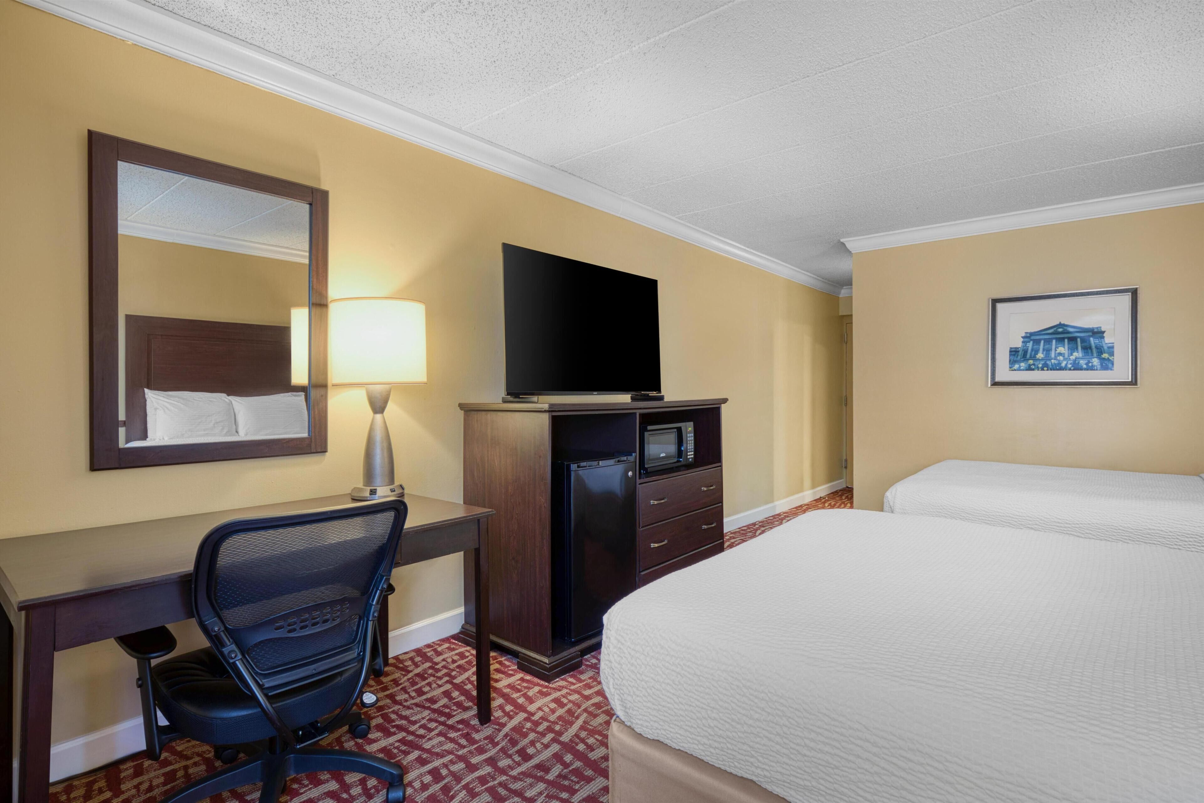 A hotel room with a bed, a desk with a chair, a television, a microwave, and a framed picture on the wall.