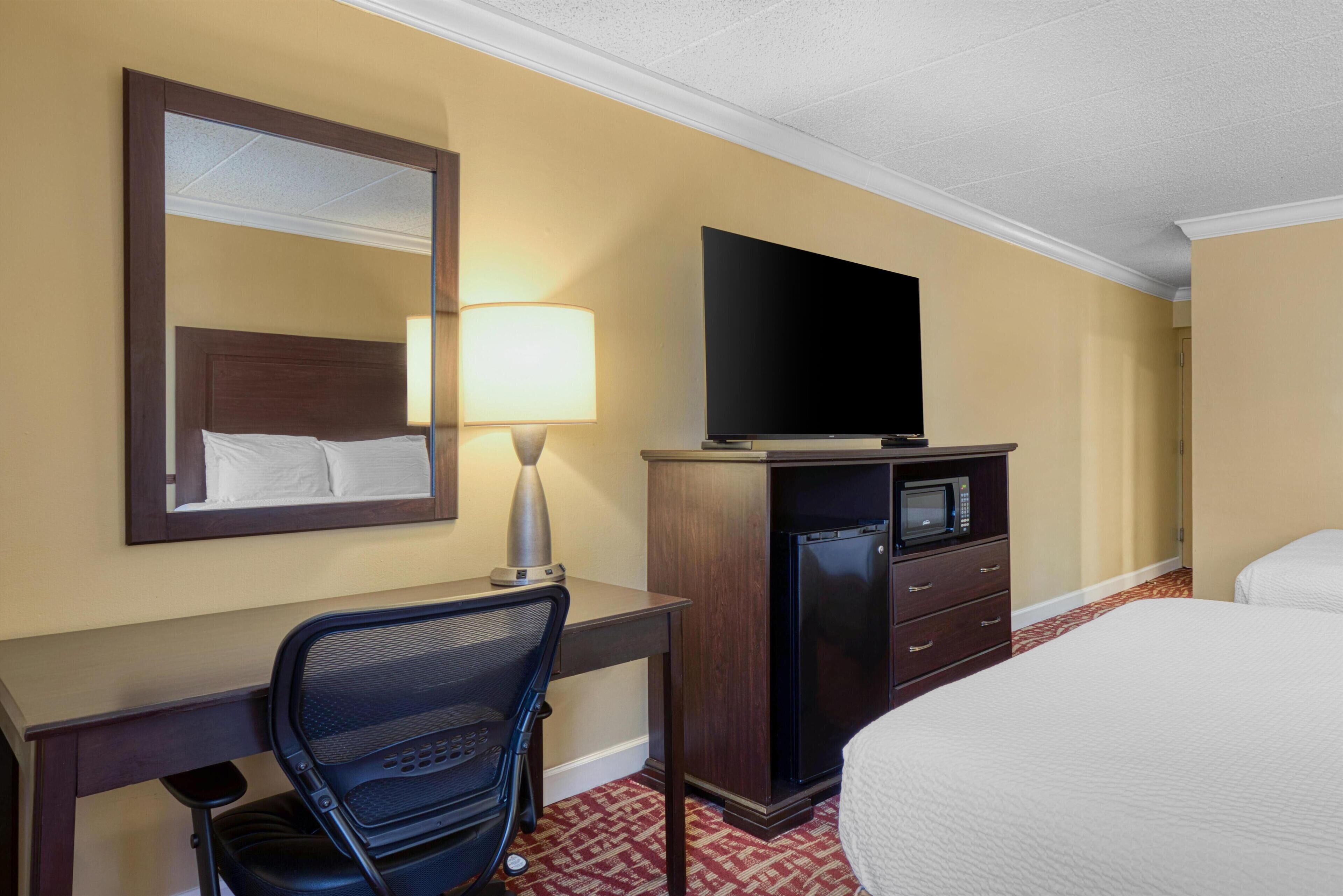 A hotel room with a bed, a desk with a chair, a television, a microwave, and a mirror.