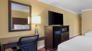 A hotel room with a bed, a desk with a chair, a television, a microwave, and a mirror.