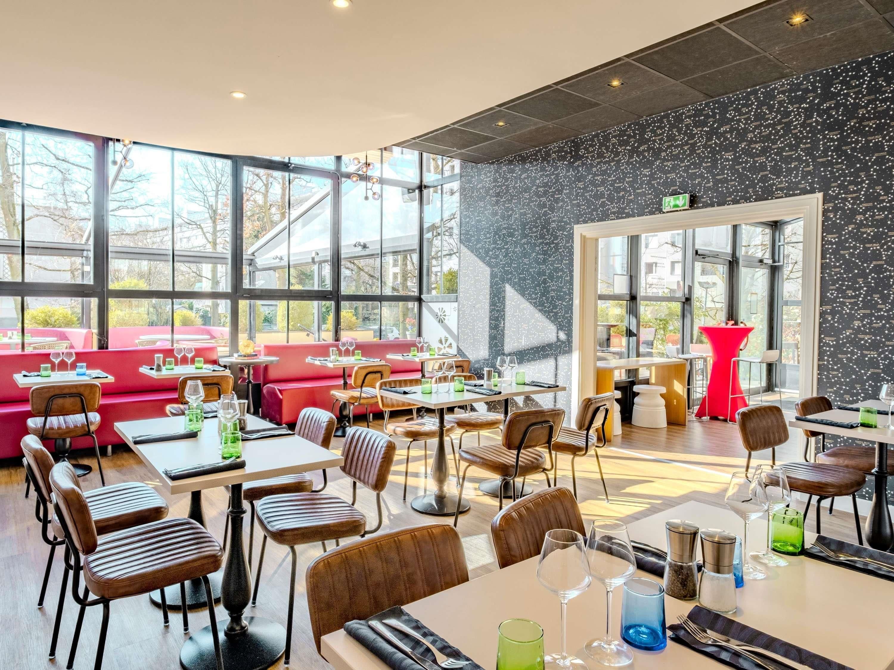 A modern restaurant with large windows, red seating, and a black speckled wall.