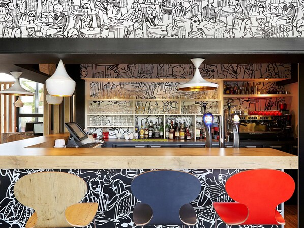 Una zona de bar con mostrador, taburetes y estantes llenos de botellas.