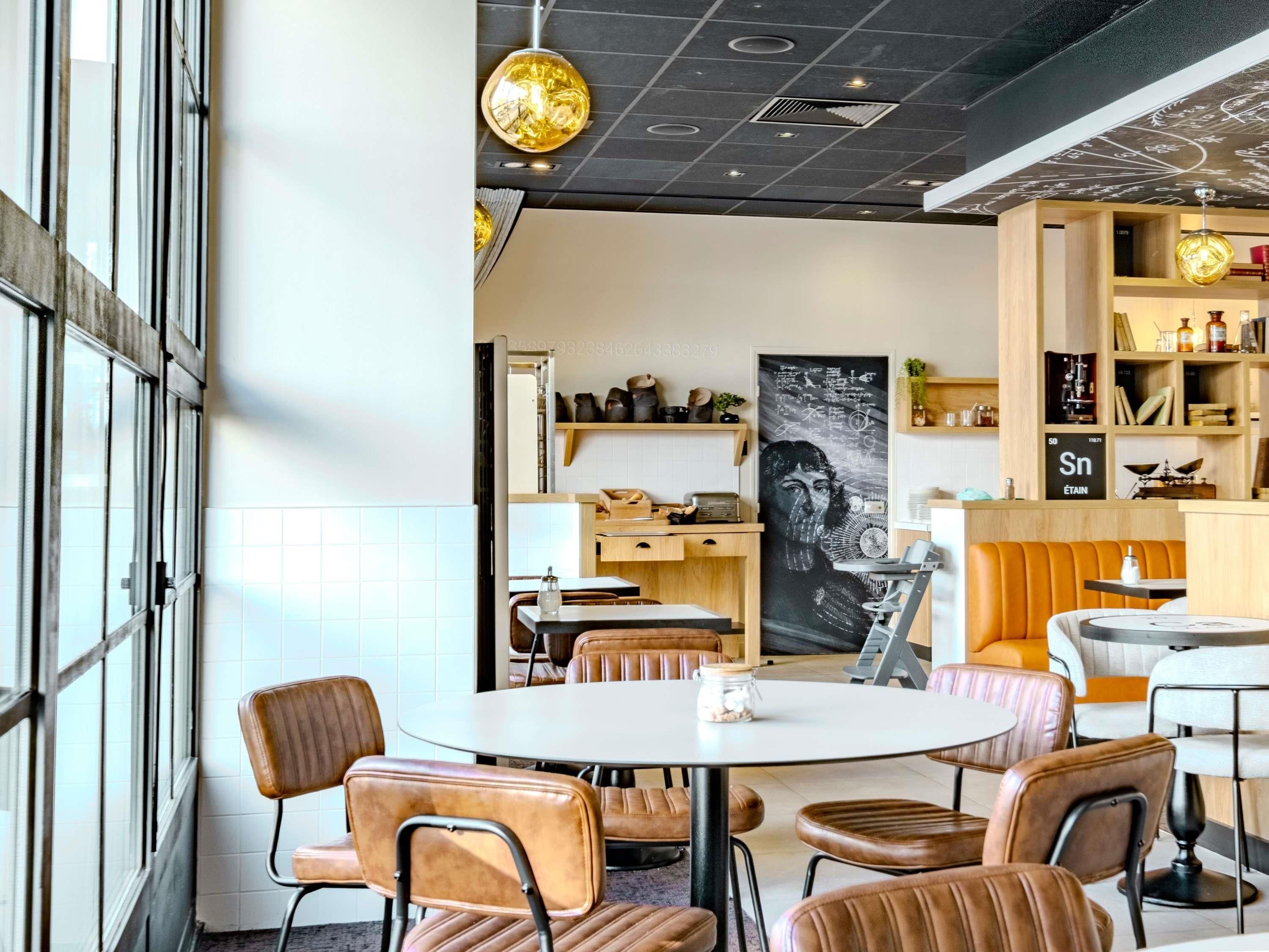 Una cafetería moderna con mesas redondas, sillas de cuero, un menú en la pizarra y una gran obra de arte en la pared.