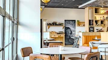 Una cafetería moderna con mesas redondas, sillas de cuero, un menú en la pizarra y una gran obra de arte en la pared.